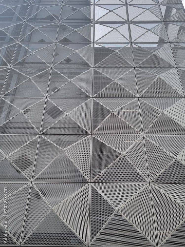 Obraz premium Close-up of a perforated metal wall with a triangular pattern on a modern building. Ideal for corporate presentations, representing transparency, structural integrity, and modern design.