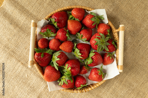 Foto Fresh strawberries filling rustic basket on burlap background