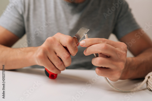 Close-up of electrician hands splitting communication cable with utility knife sitting at white table, preparing data wires for connection and installation, performing electrical repair work.