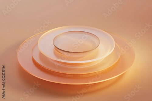Glassware layers sit atop one another in a nested arrangement within a soft studio space. Transparent discs and bowls catch warm golden light through amber tinted material with circular edges.
