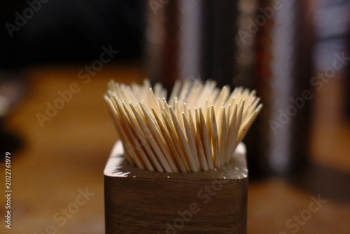 Fotografie Many light colored toothpicks stand upright in a dark wooden holder on a table indoors