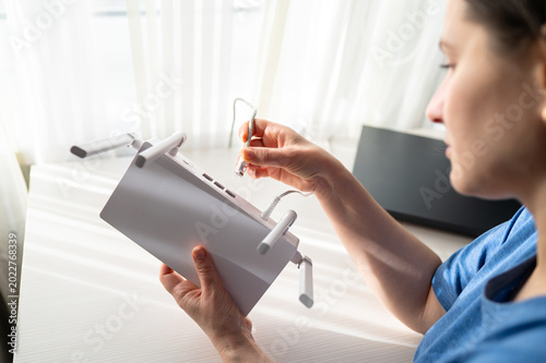 Woman Hand Plugging Network Ethernet Cable into White WiFi Router Back Panel at Home