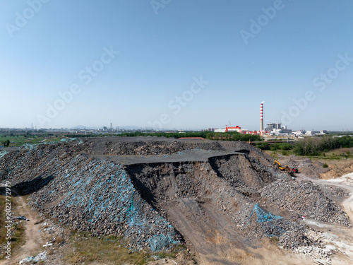 Fotografia Industrial waste slag dump site with distant power plant chimney under clear sky