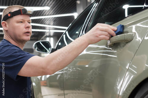 Foto The process of applying a nano-ceramic coating for hydrophobic effect on the green car's hood by a male worker with a sponge and bottle of chemical composition and microfiber