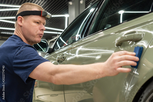Cuadro en lienzo The process of applying a nano-ceramic coating for hydrophobic effect on the green car's hood by a male worker with a sponge and bottle of chemical composition and microfiber