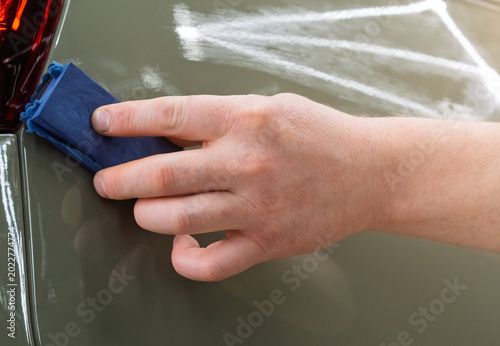 Photos The process of applying a nano-ceramic coating for hydrophobic effect on the green car's hood by a male worker with a sponge and bottle of chemical composition and microfiber