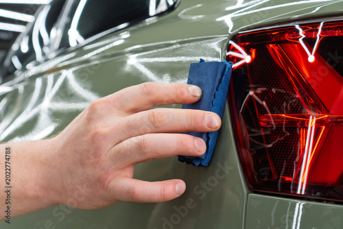 Bild auf Leinwand The process of applying a nano-ceramic coating for hydrophobic effect on the green car's hood by a male worker with a sponge and bottle of chemical composition and microfiber