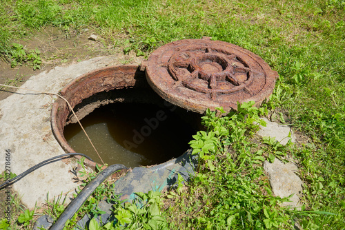 Φωτογραφία Open rusty manhole with dirty water and hose and submersible pump on lawn, An op