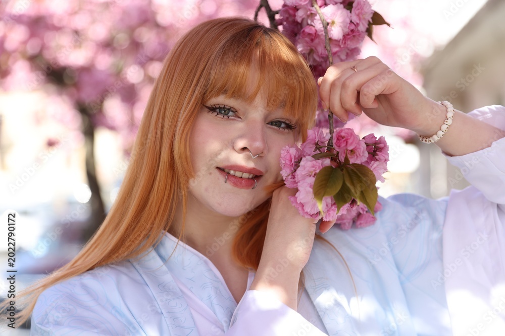 Naklejka premium Beautiful young girl in kimono posing near blossoming sakura tree outdoors