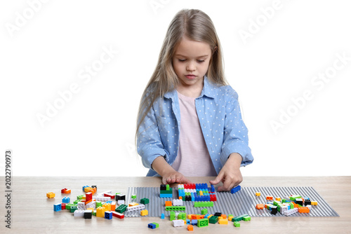 Little girl playing with colorful building blocks at wooden table against white background. Construction toy
