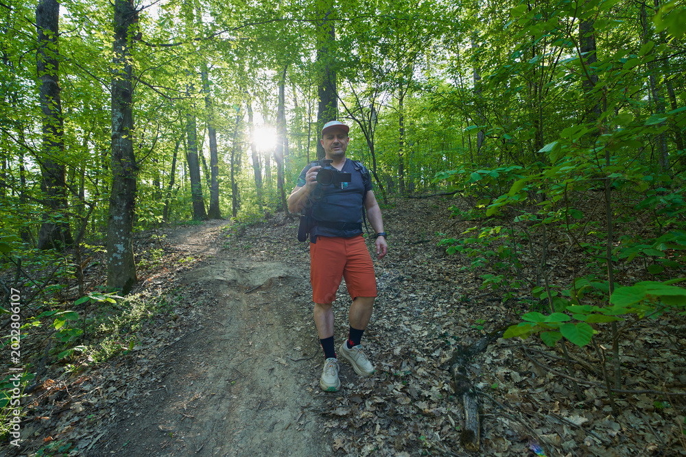 Obraz premium Man with camera hiking in backlit forest