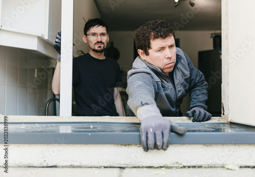 Schilderij op canvas Two handsome workers install an outdoor metal window sill.