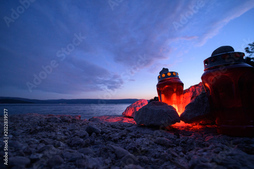 Two glowing red memorial lanterns burn on pebble beach at twilight by the sea