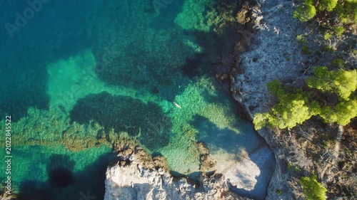 Woman floats in calm cove surrounded by rocky cliffs and clear green blue water