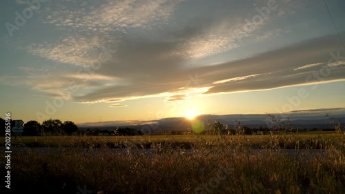Atardecer en una carretera secundaria con luz cálida de fondo y siluetas de coches pasando a contraluz.