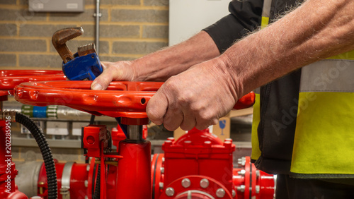 Fotografie Sprinkler system service engineer operating a red flow valve with a wrench in his hand