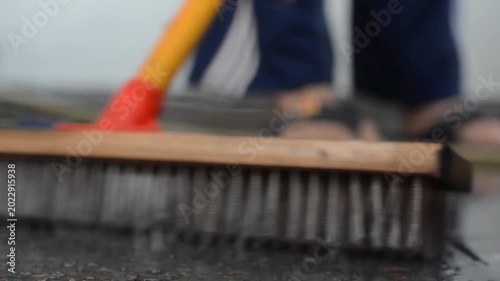 Low angle close up of a wooden brush scrubbing a wet floor outdoors during a house chore or cleaning activity