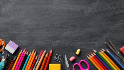 School supplies lie at bottom of dark chalkboard, forming a colorful border