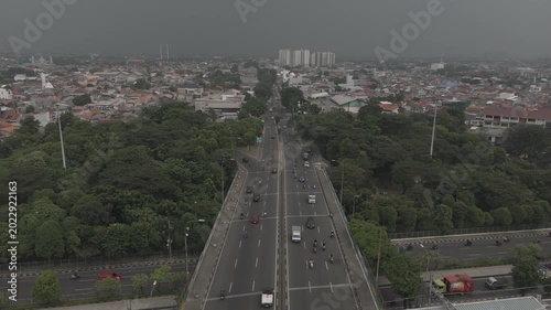 Top down aerial view of highway split with vehicles driving through lush green trees on asphalt road