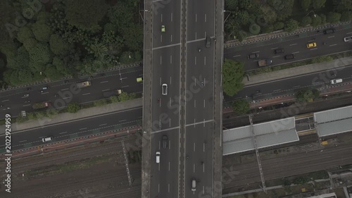 Aerial top-down view of a flyover highway with traffic crossing over a train station platform in Jakarta, Indonesia