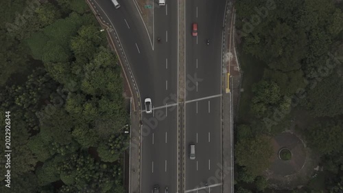 Top down aerial view of highway intersection with moving cars and green trees in city