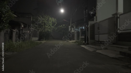 Quiet empty suburban street at night under a single bright streetlight with puddles after rain