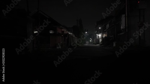 Quiet and dark suburban residential street at night illuminated by distant streetlights under a dim sky