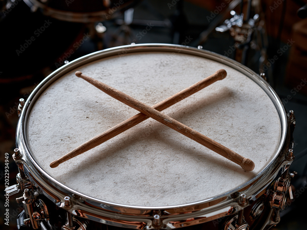 Fototapeta premium Crossed Wooden Drumsticks on Snare Drum with Detailed Rim and Dark Studio Background