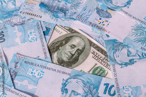 One hundred American dollar bill, stuck between 100 Brazilian real bills. Economic crisis and drop in the American currency