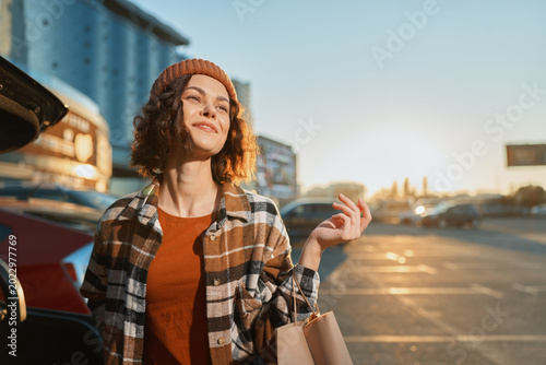 Canvastavla Woman shopping by car in a parking lot at sunset, portrait with shopping bags and relaxed smile conveying authenticity, candid lifestyle, golden hour glow and mindful living