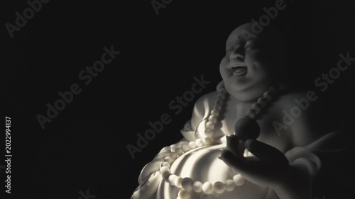 A white smilling Buddha statue illuminated by a flickering light in the darkness