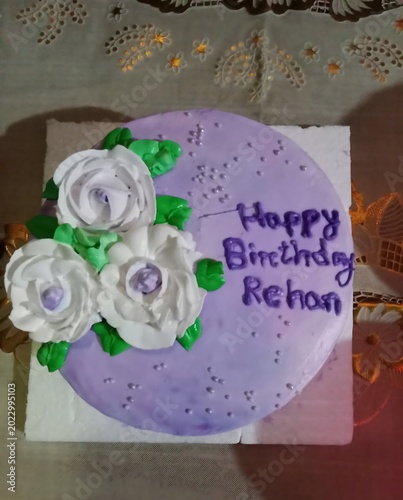 round birthday cake with purple frosting white flowers and happy birthday message