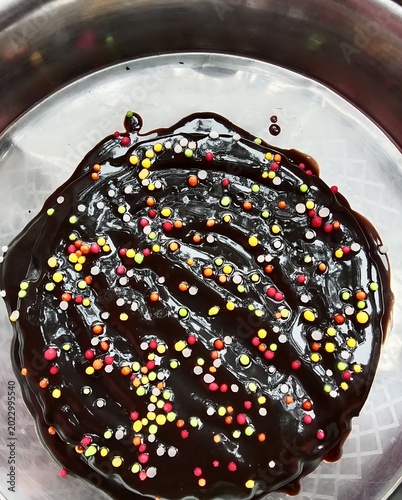 round chocolate cake with glossy glaze and colorful sprinkles in metallic container
