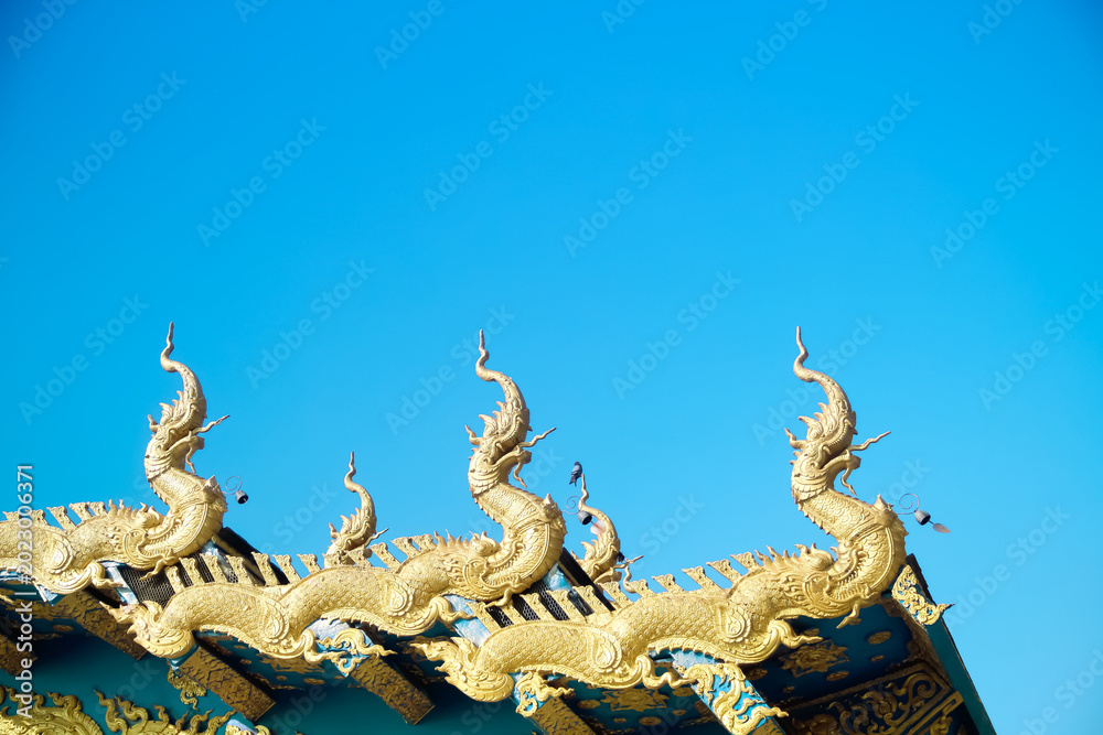Fototapeta premium Gold naga patterns decorative on roof Thai temple on bright blue sky background