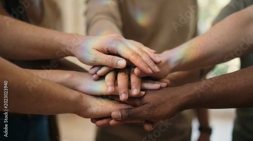 Group of diverse hands stacked together with soft rainbow light overlay