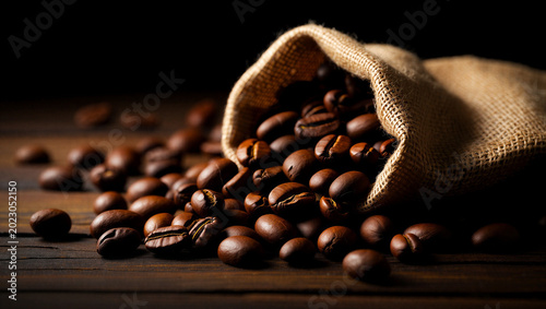 Obraz na płótnie Roasted coffee beans spilling from burlap sack on dark wooden table with moody
