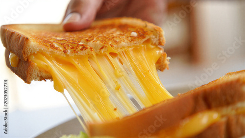 Fotografie Person pulling apart melted cheese grilled sandwich on white bread with golden