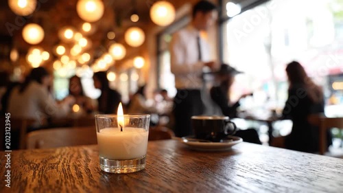 Cozy Restaurant Interior with Flickering Candle on a Wooden Table and Blurry Patrons Enjoying Coffee in Soft Warm Lighting