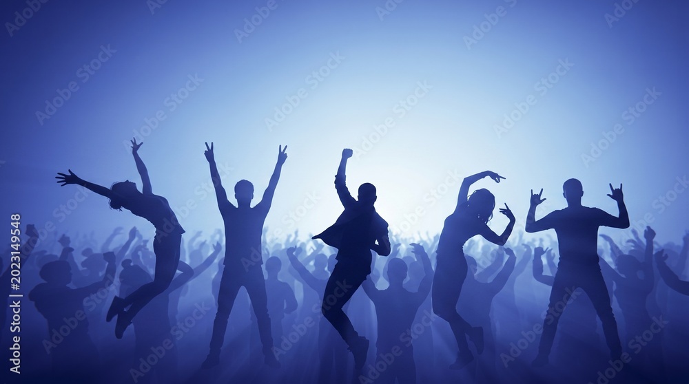 Fototapeta premium Group of people dancing and celebrating at a nighttime concert with hands raised