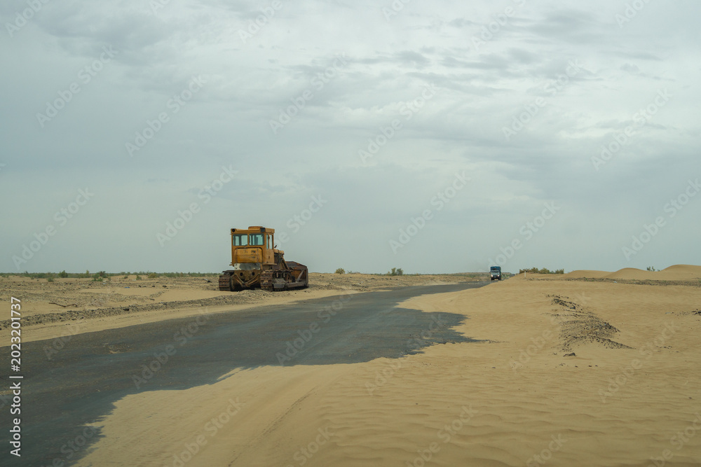 Fototapeta premium A lonely bulldozer and distant truck sit on a remote Kyzylkum desert road from Bukhara to Khiva, Uzbekistan.