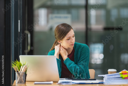 Young businesswoman rubbing her neck feeling pain and stiffness from office syndrome while working on laptop.