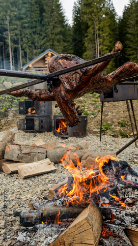 Foto Whole lamb roasting over an open fire in a rustic mountain setting