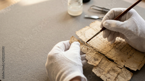 Restoration of ancient manuscript by professional conservator wearing white cotton gloves
