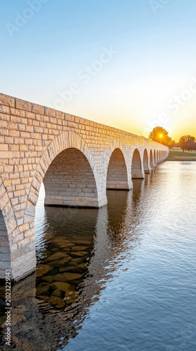 Historic stone bridge at sunset over calm water with arches and golden light