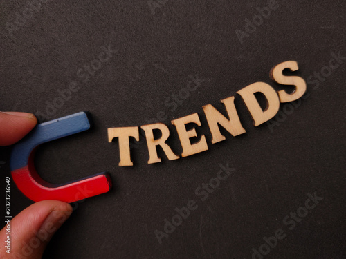 A hand holds a horseshoe magnet pulling wooden letters that spell TRENDS on a black surface