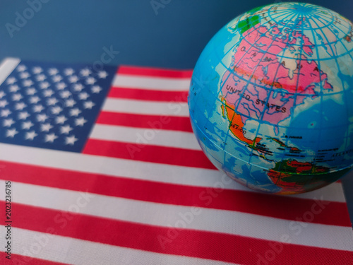 A small globe showcasing North America sits on top of a flag of the United States