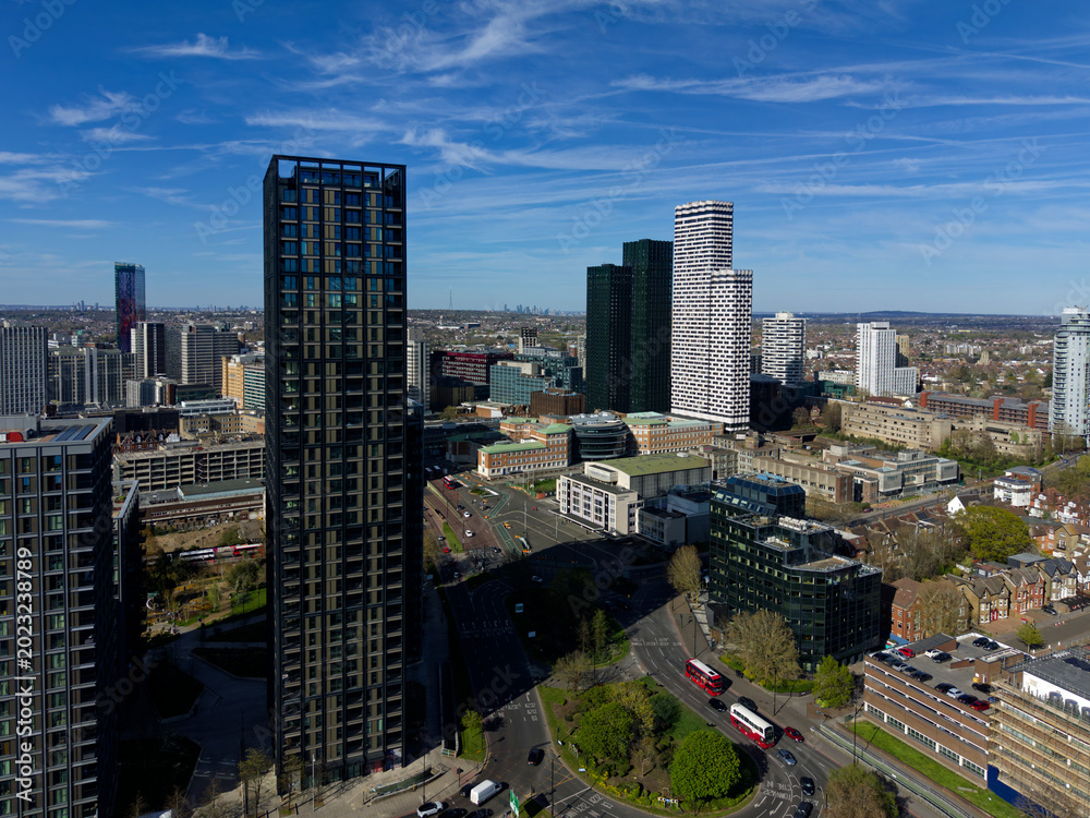Obraz premium Red public buses at roundabout in Croydon aerial view. Modern architecture with tall skyscrapers in town center. Quiet roads in business district on a sunny day with blue sky.