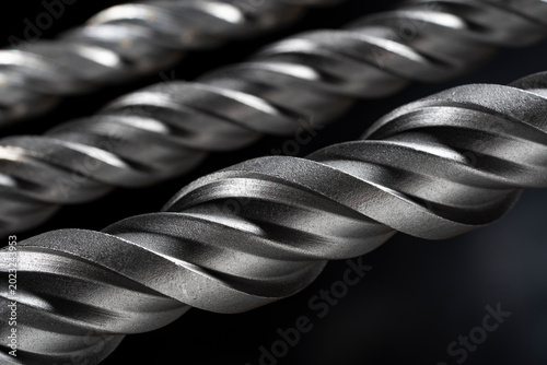 Macro steel spiral drill bit texture on dark background. Metal drill bit spiral flutes on black background. Concept of industrial tools engineering precision construction and hardware equipment