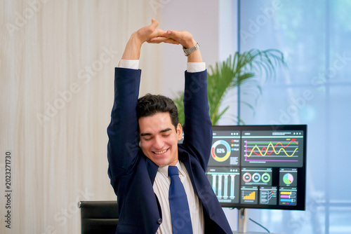 Businessman in navy suit stretch oneself on his desk office with monitor graphic information , relax from hard work and avoid office syndrome.