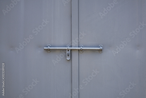Fotografia Twin muted‑gray industrial doors with padlock hasp mounted on single gray slide bolt